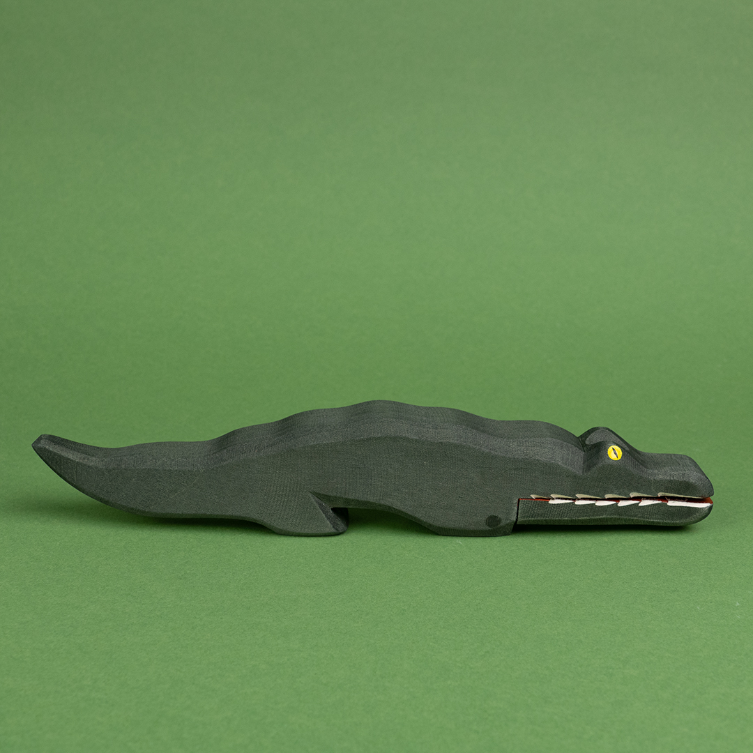 Ein dunkelgrünes Krokodil aus Holz ist in der Seitenansicht zu sehen. Es hat gelbe Augen und weiße, lange Zähne und ist von der Marke Ostheimer.