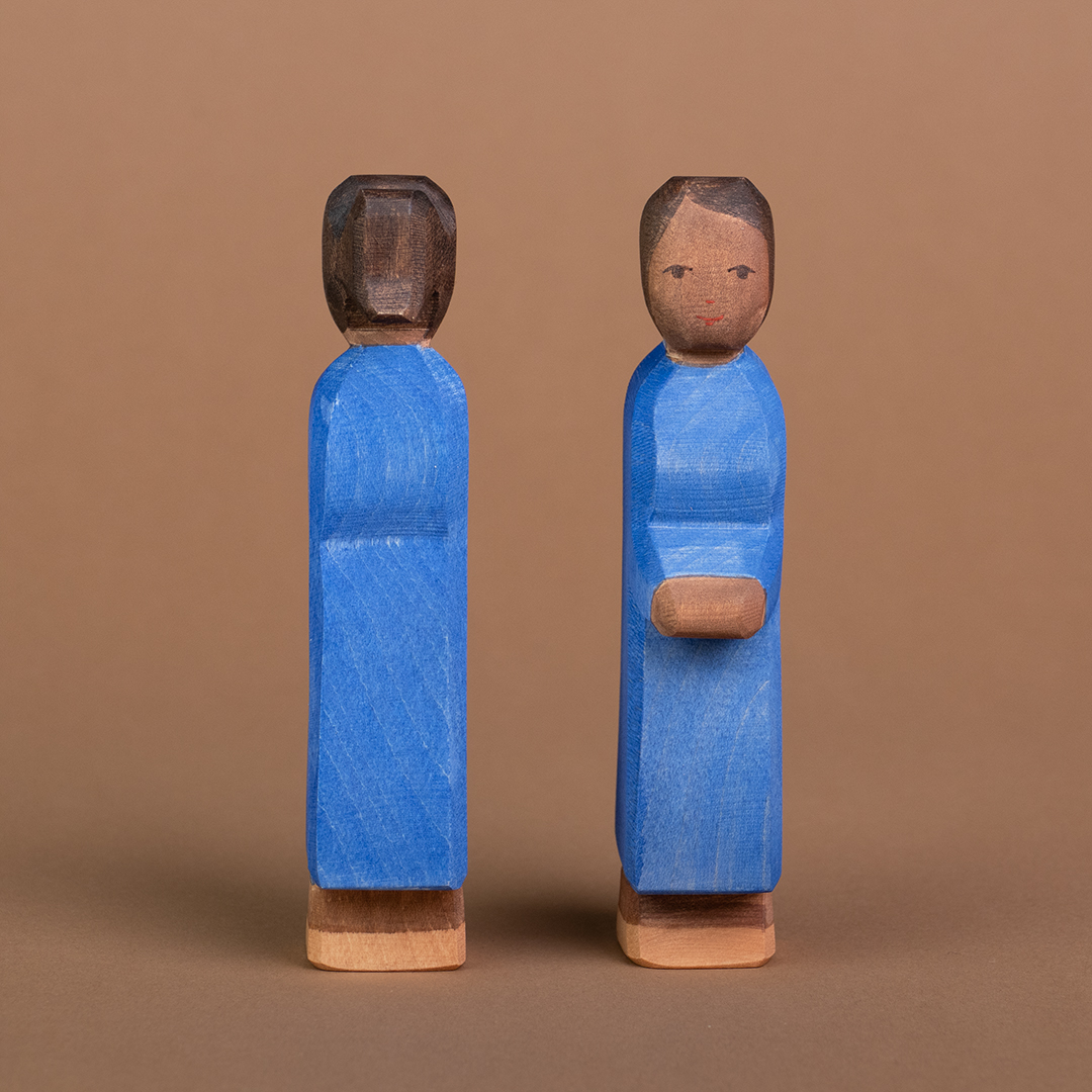 Zwei Mütter aus Holz mit dunkler Hautfarbe sind nebeneinander parallel stehend zu sehen. Die rechte Mutter schaut nach vorne und ist mit dem Gesicht zu sehen, die linke Mutter schaut nach hinten und ist nur von hinten zu sehen.