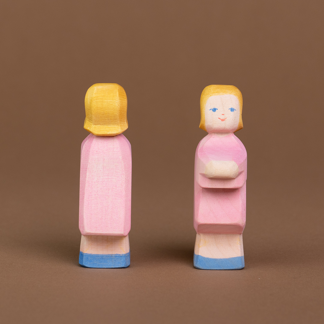 Zwei Töchter aus Holz sind nebeneinander parallel stehend zu sehen. Die rechte Tochter schaut nach vorne, die linke schaut nach hinten und ist nur von hinten zu sehen.
