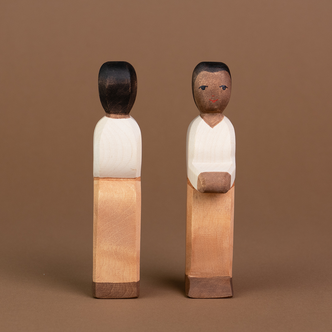 Zwei Väter aus Holz mit dunkler Hautfarbe sind nebeneinander parallel stehend zu sehen. Der rechte davon ist von vorne zu sehen, der linke ist von hinten zu sehen, von der Marke Ostheimer.