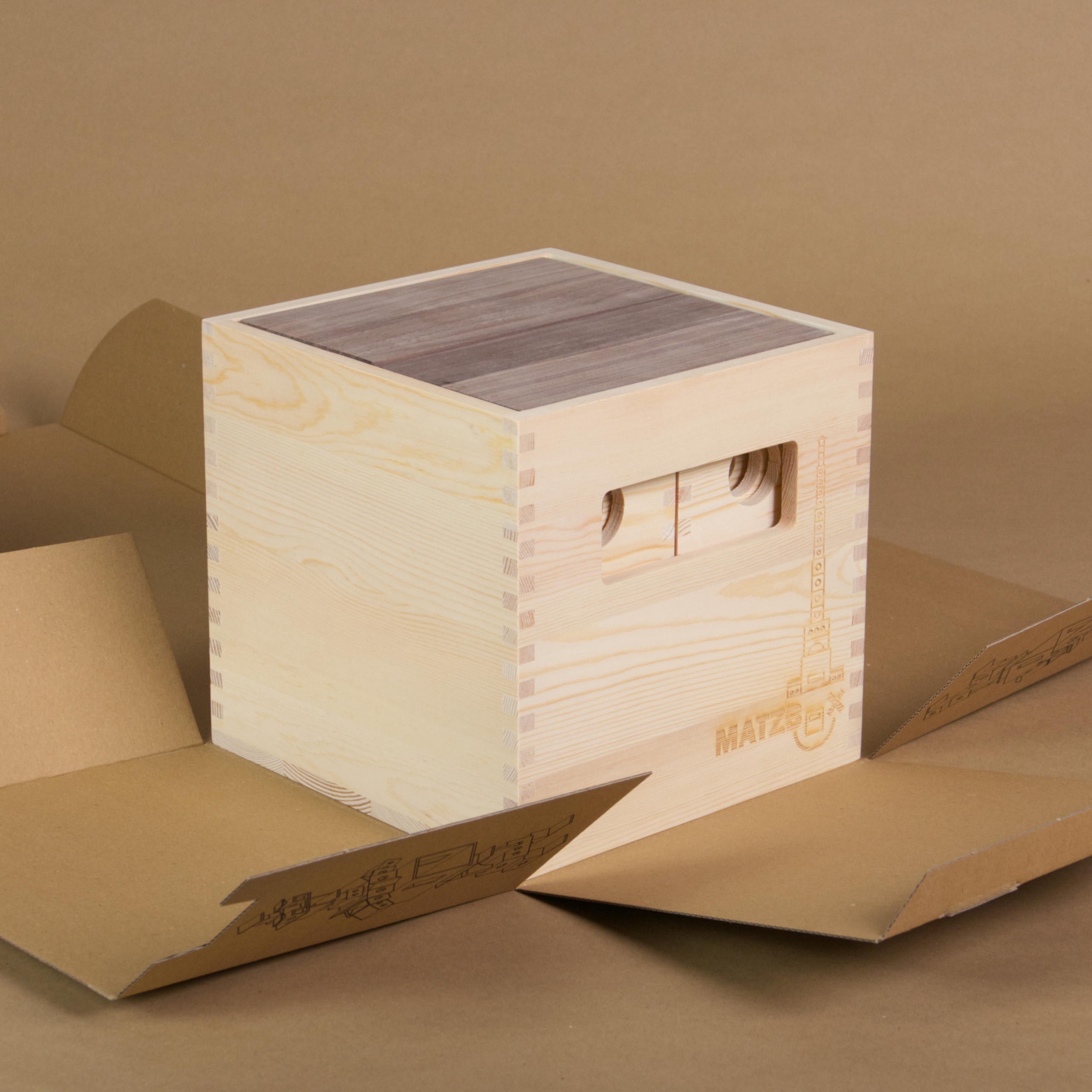 Die MATZBOX steht auf der originalen Pappverpackung, welche bereits aufgefaltet ist. Die Elemente der Matzbox sind alle in die offene Holzkiste aus hellem Holz eingesortiert.
