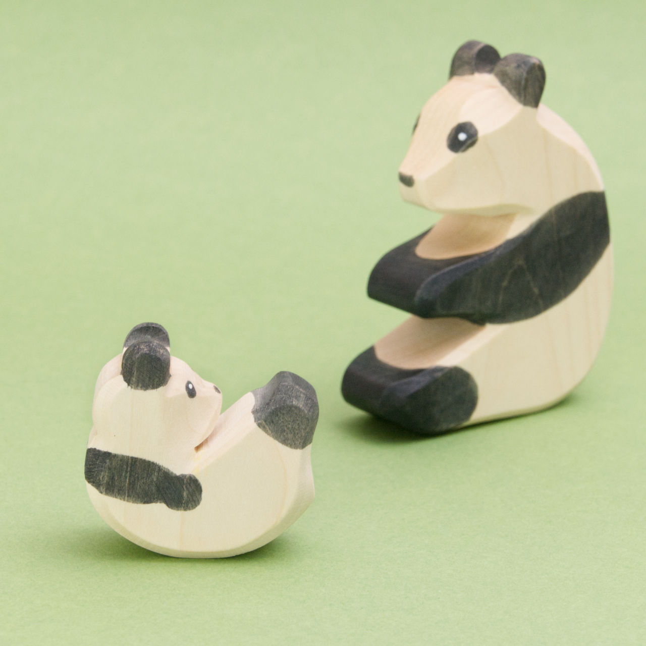 Hier sind zwei holz Panda Bären zusehen, wobei das PandaBaby das zu dem sitzenden Panda hinaufschaut. Die handgemachten Holzsbären für Jungs und Mädchen haben schwarze Ohren. Durch die sichtbare Buchenholz Maserung ist erkennbar, es handelt sich um deutsche, ungiftige Holzfiguren.