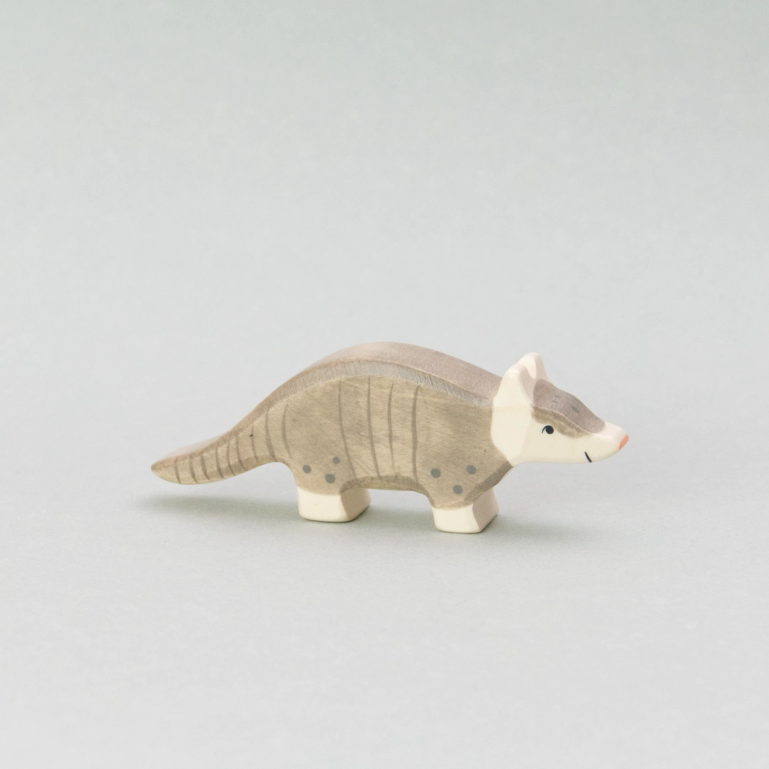 Das Gürteltier von Holztiger ist eine detailreiche Holzfigur mit handbemalter Oberfläche. Das Spielzeug-Holztier hat einen grauen Körper mit aufgemalten Gürtellinien, die seinen typischen Panzer nachbilden. Der Kopf und die Beine sind in einem sanften Cremeweiß gehalten, während die kleine, spitz zulaufende Nase in einem zarten Rosa leuchtet. Die Figur hat eine geschwungene Körperhaltung und steht stabil auf vier Beinen – ideal für kreatives Spielen oder als dekorative Ergänzung in einer Tierwelt-Sammlung.