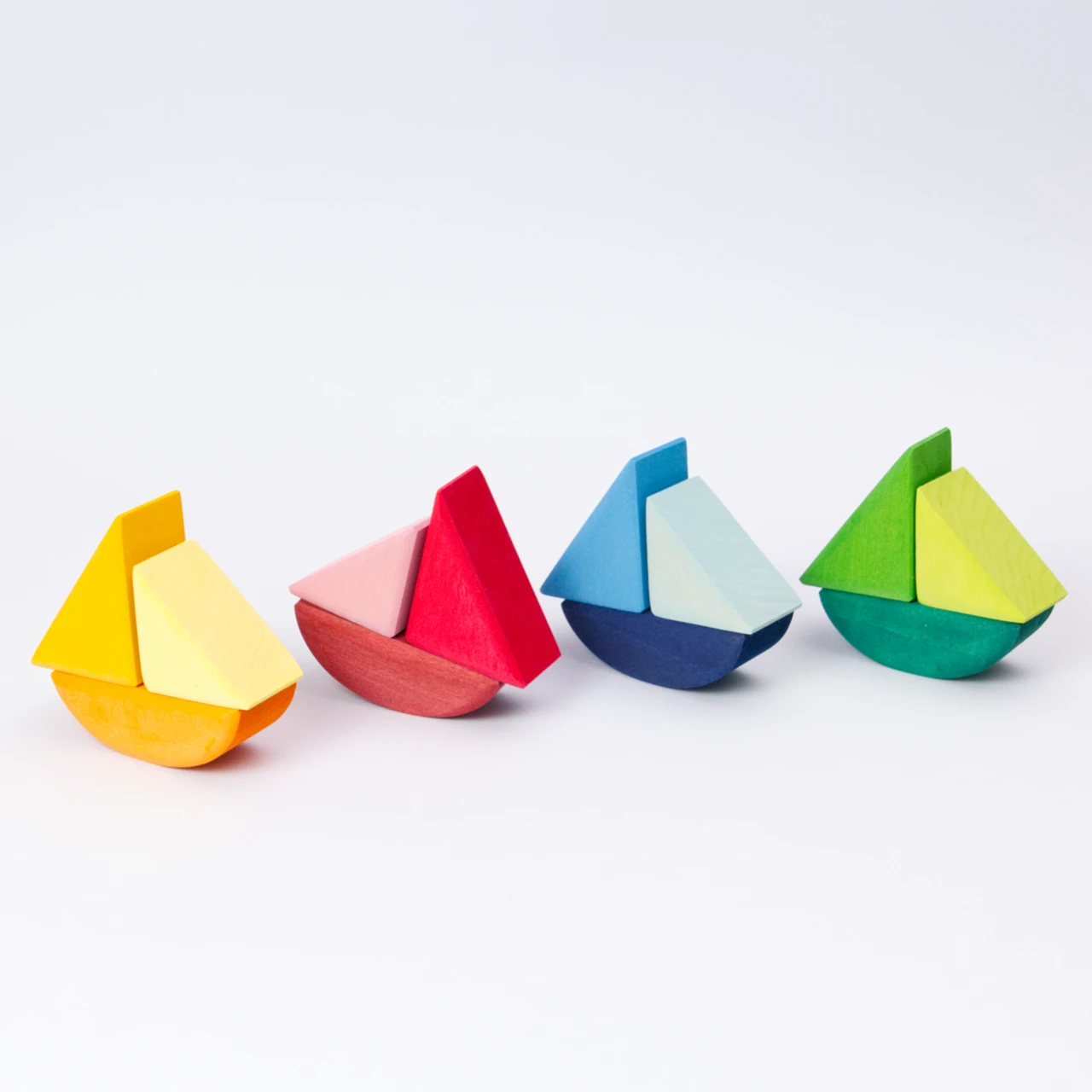 Schaukelschiffe, aus drei Teilen, von Grimms aus Holz zum Spielen, in verschiedenen Farbtönen von gelb, rot, blau und grün. In einer Reihe schräg aufgestellt.