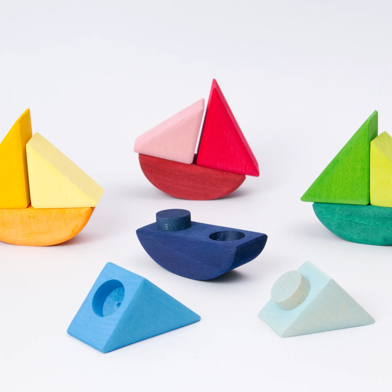 Schaukelschiffe, aus drei Teilen, von Grimms aus Holz zum Spielen, in verschiedenen Farbtönen von gelb, rot, blau und grün. Das blaue Schiff ist in drei Einzelteilen zerlegt.