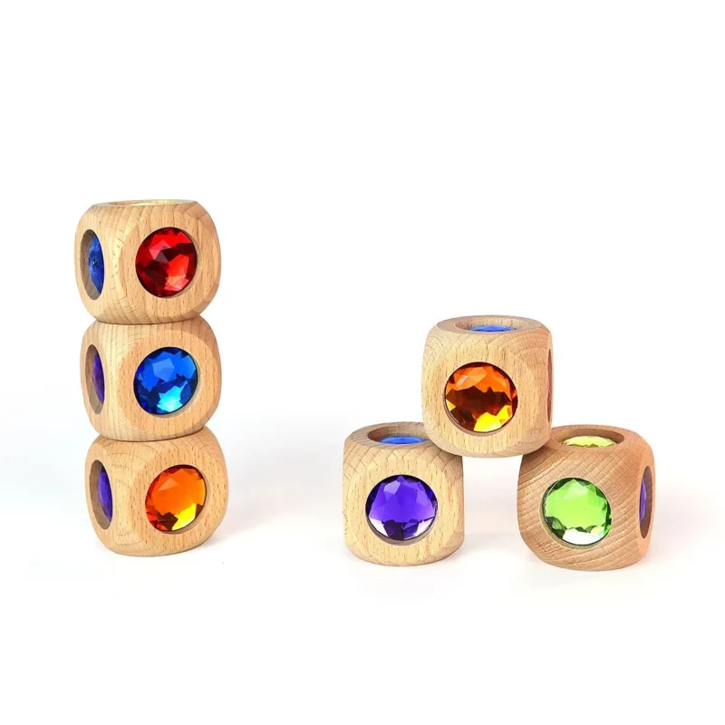 Eine Gruppe von mehreren Exemplaren des Zauberwürfels vom Hersteller Bauspiel. Ein Farbwürfel aus Holz mit bunten Juwelen aus Acrylglas. Hier sind drei Würfel aufeinander gestapelt zu einem Turm zu sehen, sowie drei weitere zu einer Pyramide aufgetürmt. Zu sehen sind auch die bunten Acrylsteine an den Würfelflächen in den Farben: Blau, Violett, Rot, Orange, Grün und Gelb.